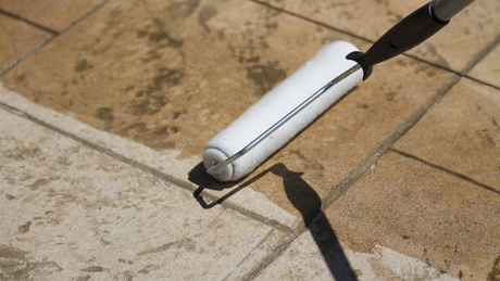 A paint roller applying sealer to a tiled outdoor patio.