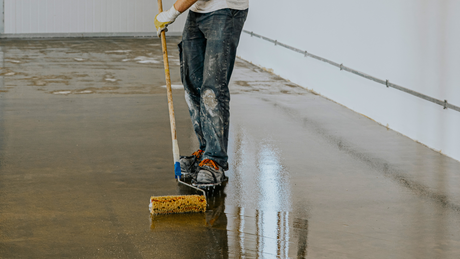 A person applying floor paint with a roller on a concrete surface.