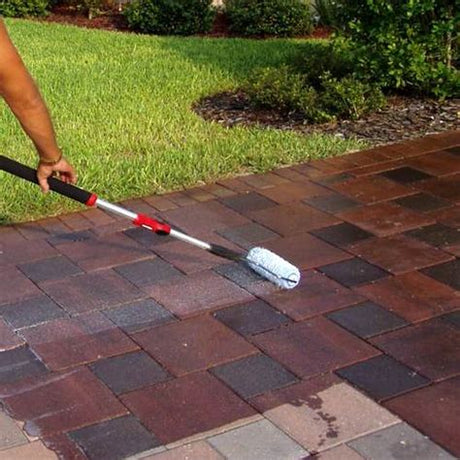 A person applying patio sealer with a roller on a brick patio.